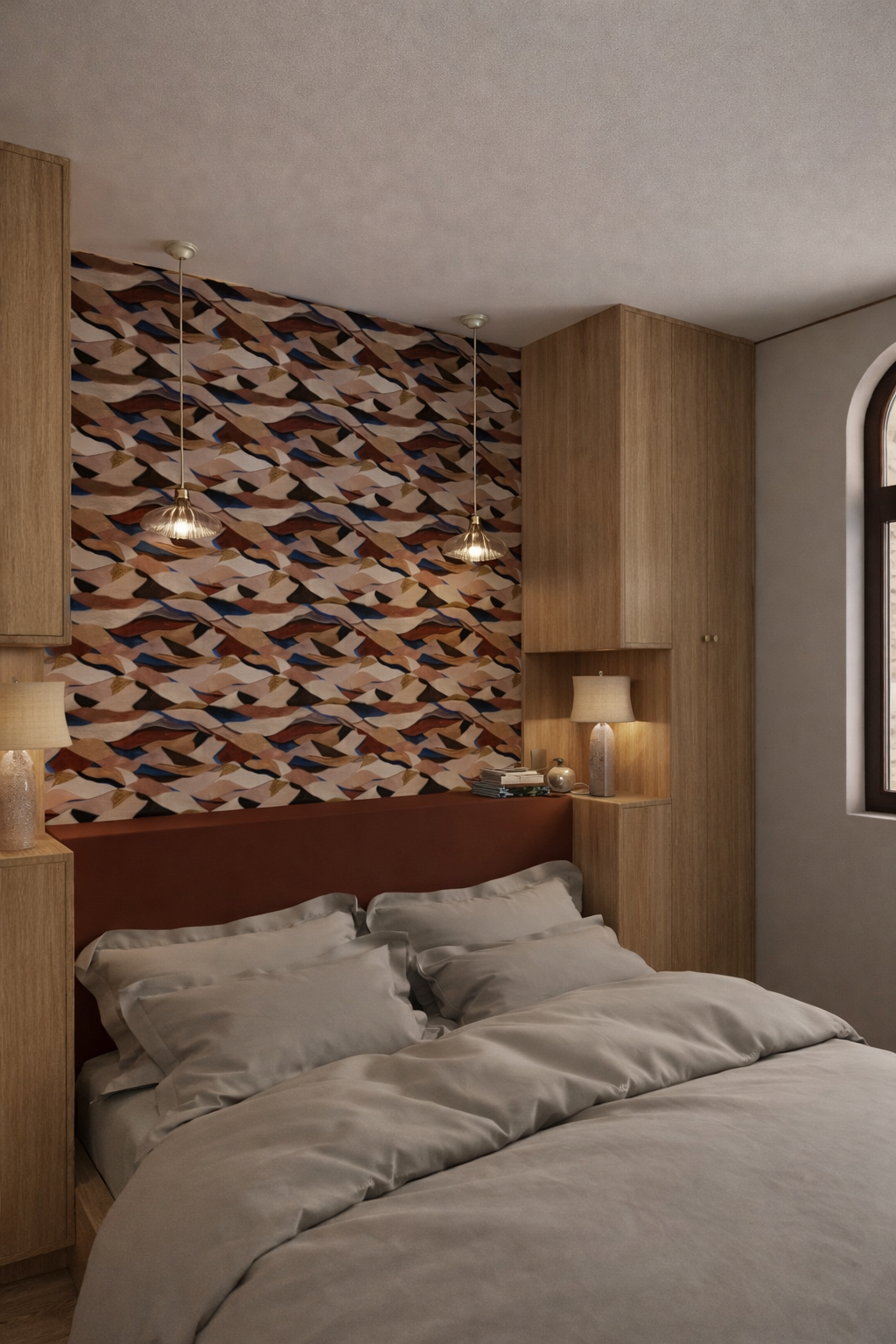 Chambre avec mur de tête de lit tapissé d’un papier peint à motif abstrait multicolore, tête de lit bordeaux, rangements en bois clair et fenêtre cintrée